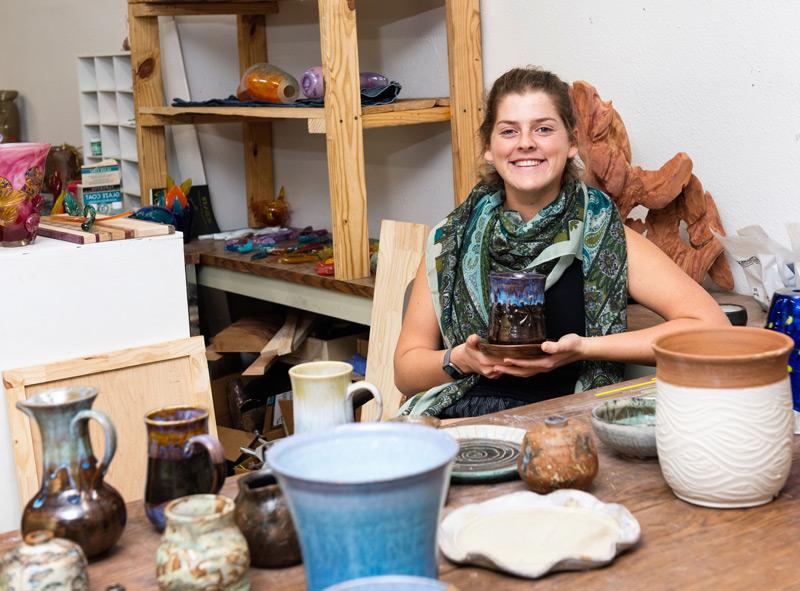 Student in the ceramics studio surrounded by ceramic and glass artwork.